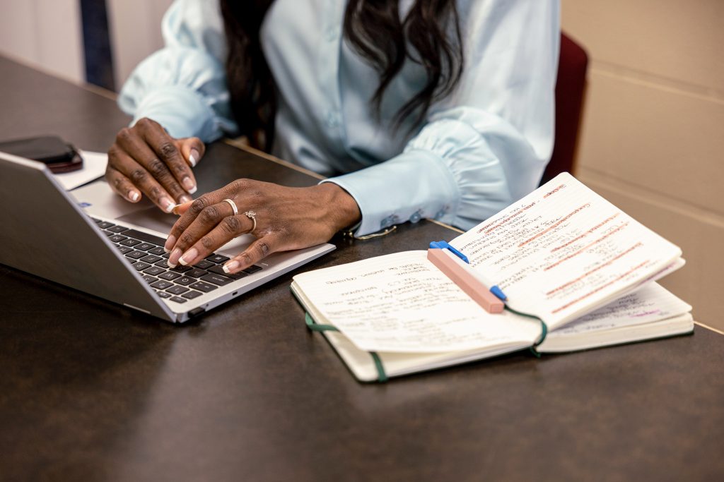 Photograph of Jasmine Ames typing on her laptop next to her open note book