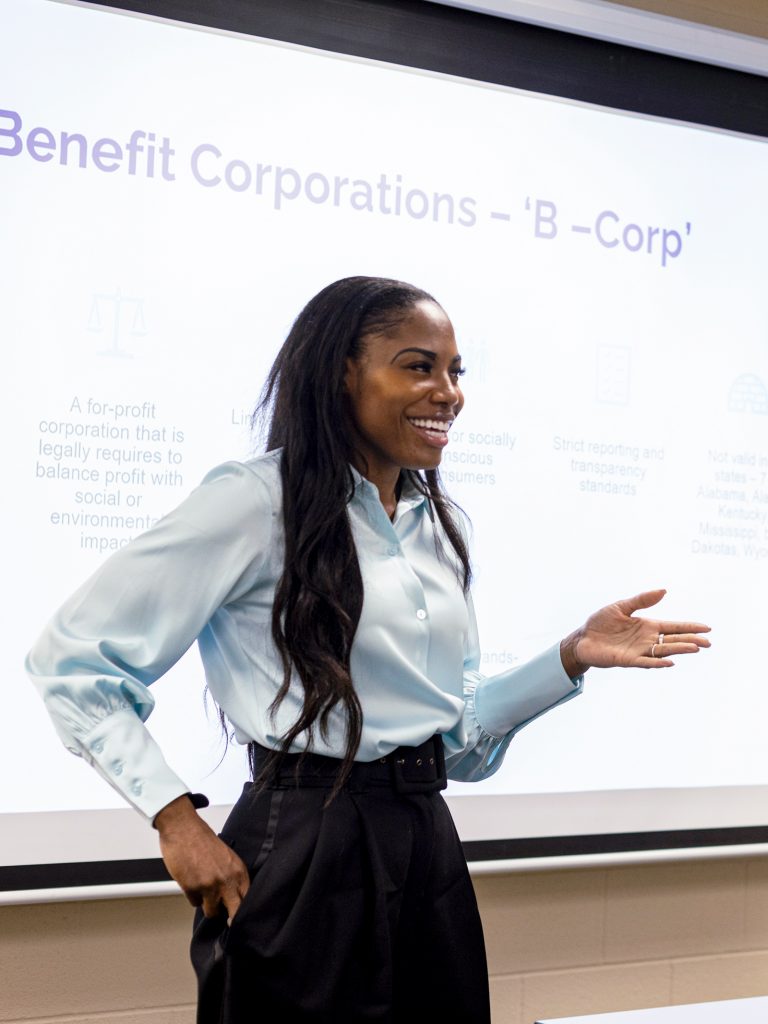 A photograph of Jasmine Ames in front of a projector delivering a presentation on B Corp